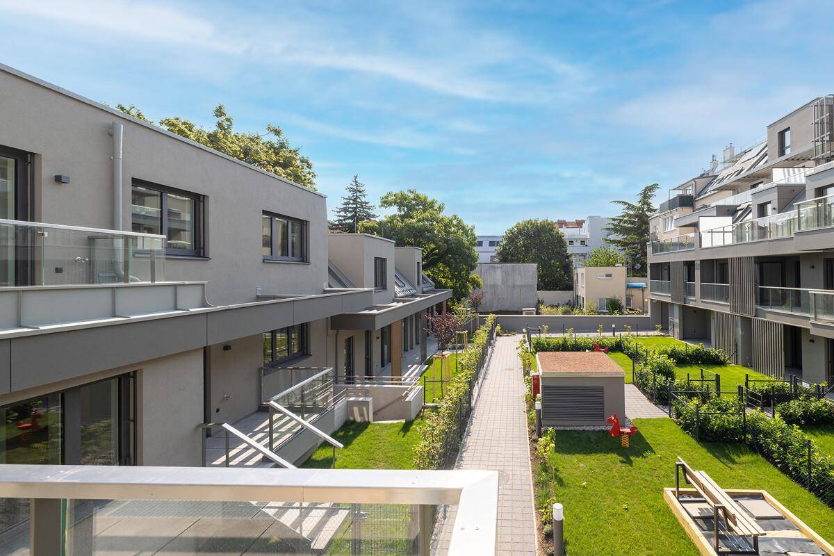 Weitläufiger Gemeinschaftsgarten mit Grünflächen und modernen Wohngebäuden im Hintergrund.