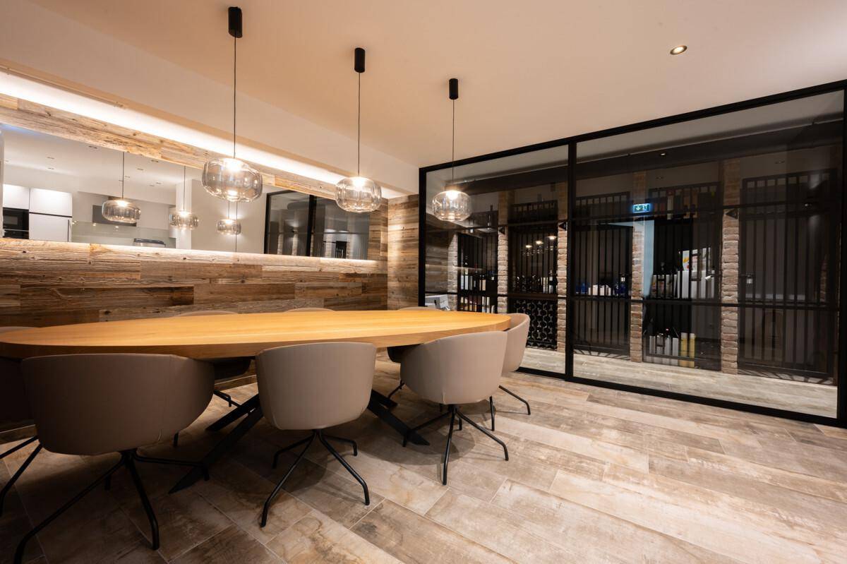 Eleganter Essbereich mit Holztisch, modernen Pendelleuchten und einem integrierten Weinkeller hinter Glas.