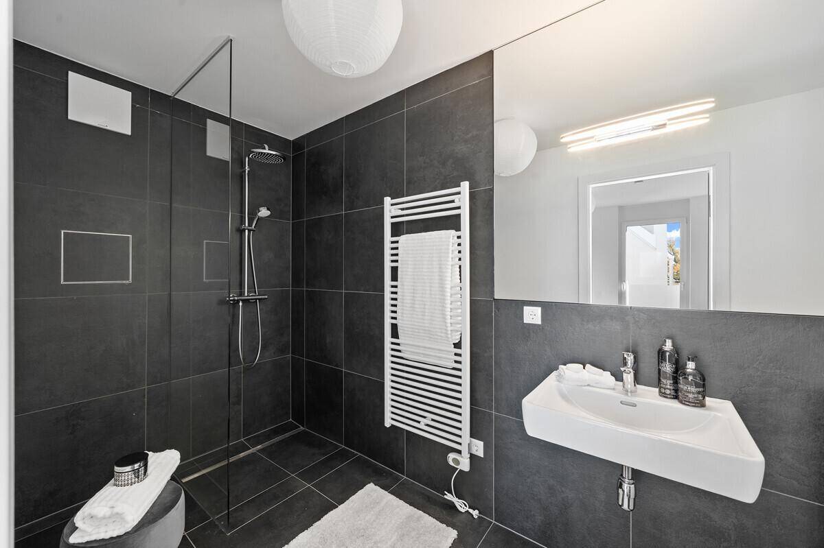 Modernes Badezimmer mit dunklen Fliesen, ebenerdiger Dusche und beheiztem Handtuchhalter.