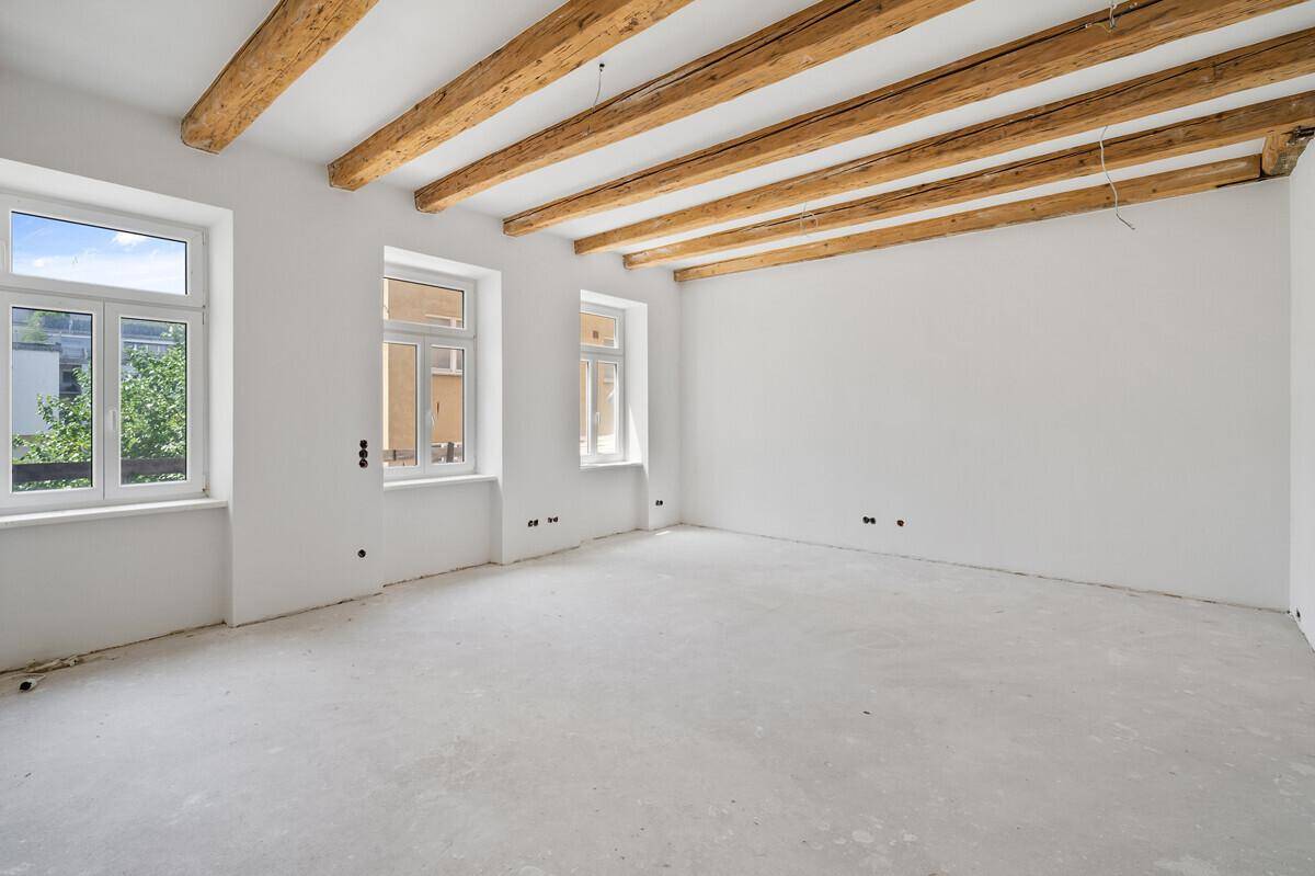 Großer, lichtdurchfluteter Raum mit sichtbaren Deckenbalken, bereit für den Ausbau.