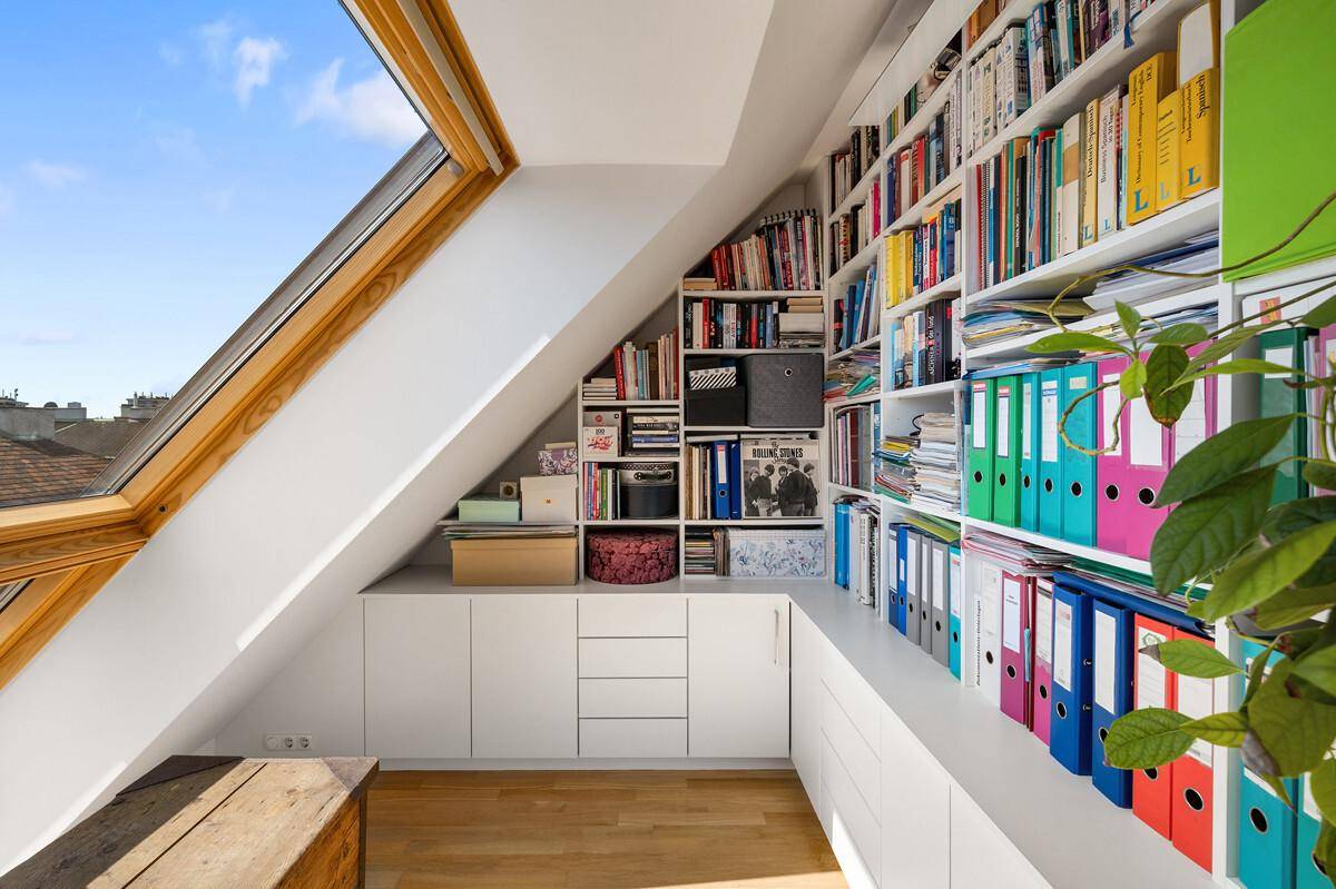 Helles Arbeitszimmer im Dachgeschoss mit umfangreichen Bücherregalen und Dachfenster.