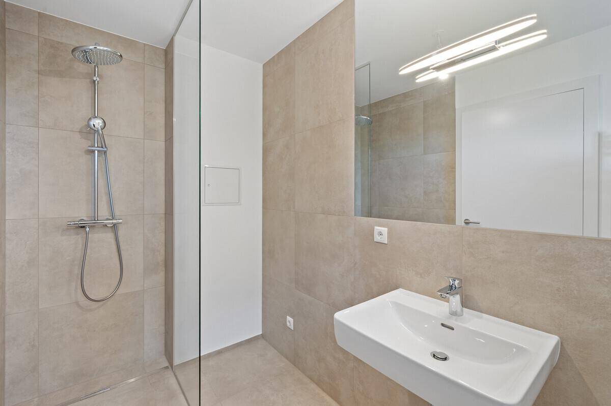 Modernes Badezimmer mit beigefarbenen Fliesen, einer ebenerdigen Dusche und einem einzelnen Waschbecken.