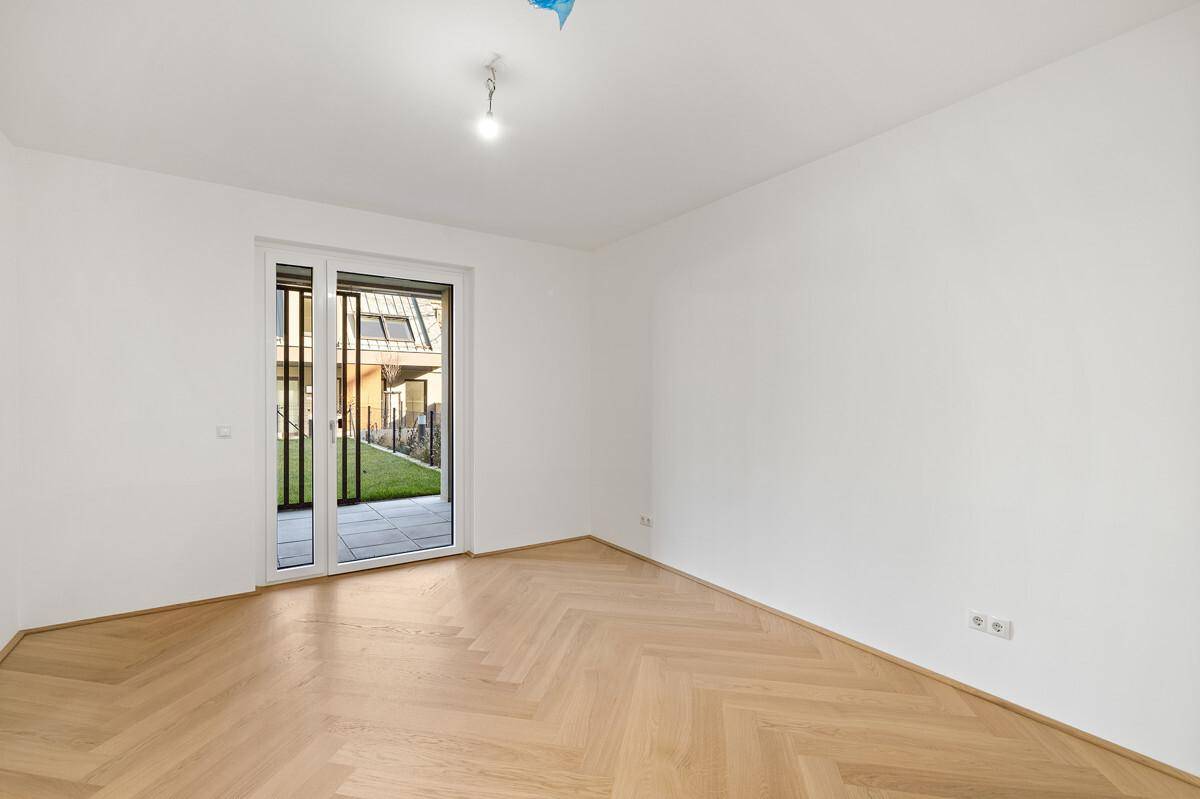 Geräumiges Zimmer mit hellem Fischgrätparkett und Zugang zu einem Außenbereich.