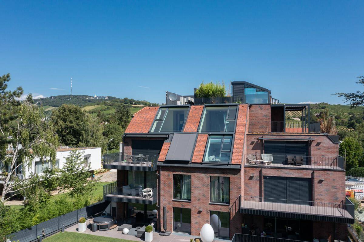 Modernes Mehrfamilienhaus mit Ziegelfassade, großen Fenstern und mehreren Balkonen und Dachterrassen.