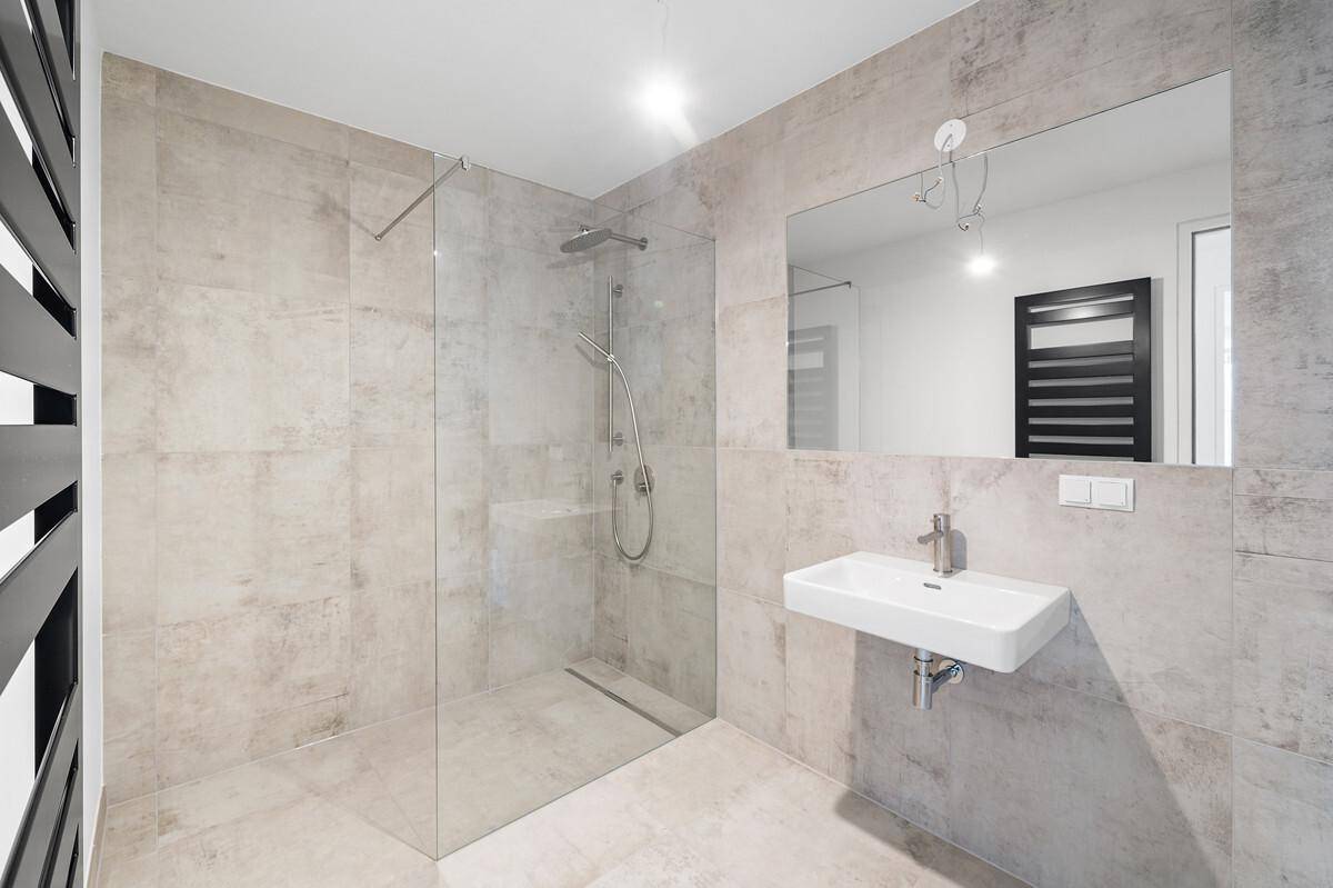 Modernes Badezimmer mit großformatigen grauen Fliesen, ebenerdiger Dusche und Einzelwaschbecken.