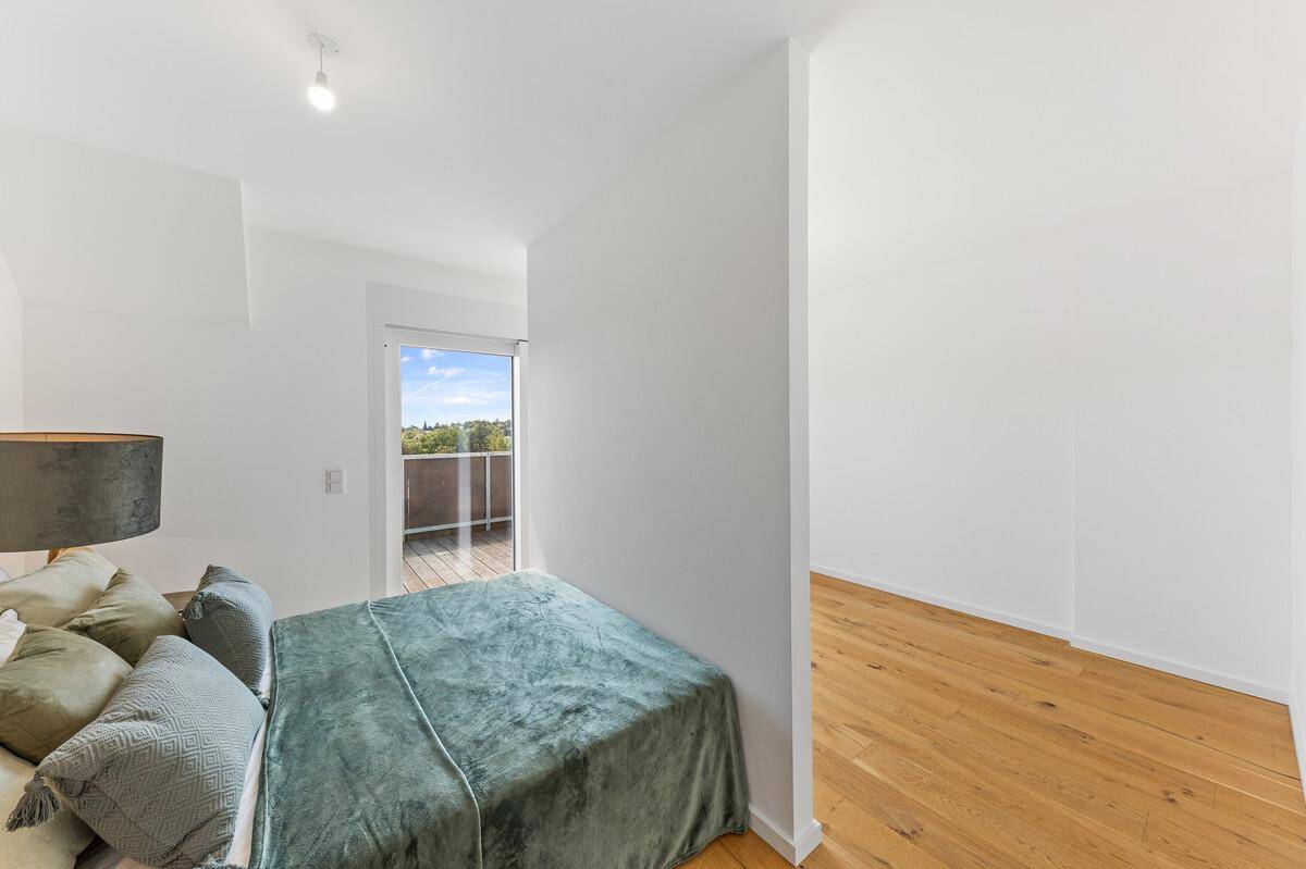 Helles Schlafzimmer mit Zugang zu einem Balkon und Blick ins Grüne.