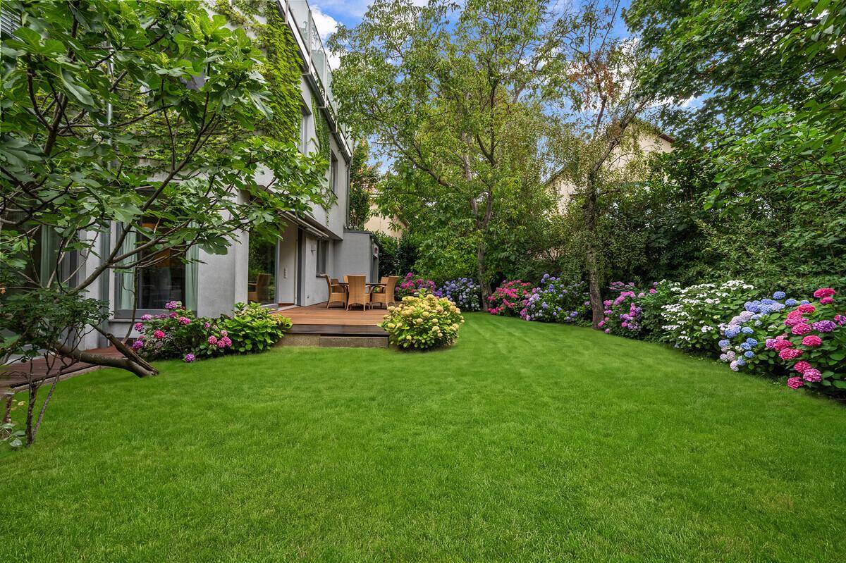Weitläufiger, gepflegter Garten mit großer Rasenfläche und üppigen Blumenbeeten hinter dem Haus.