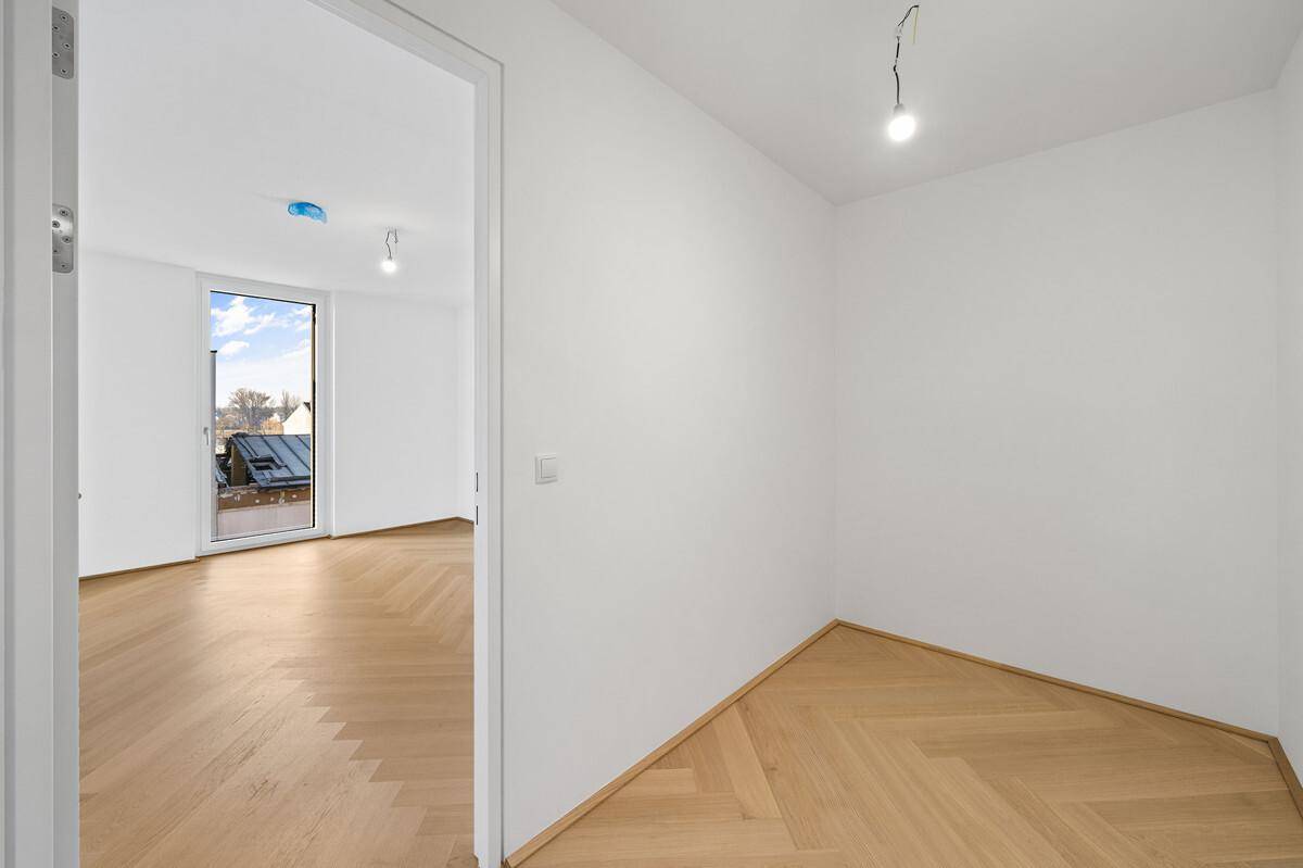 Heller Flur mit Fischgrätparkett, der zu einem weiteren Zimmer mit Balkonzugang führt.