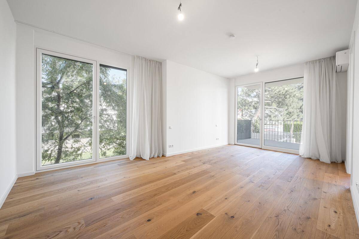 Lichtdurchflutetes Wohnzimmer mit Holzboden, raumhohen Fenstern und Blick ins Grüne.