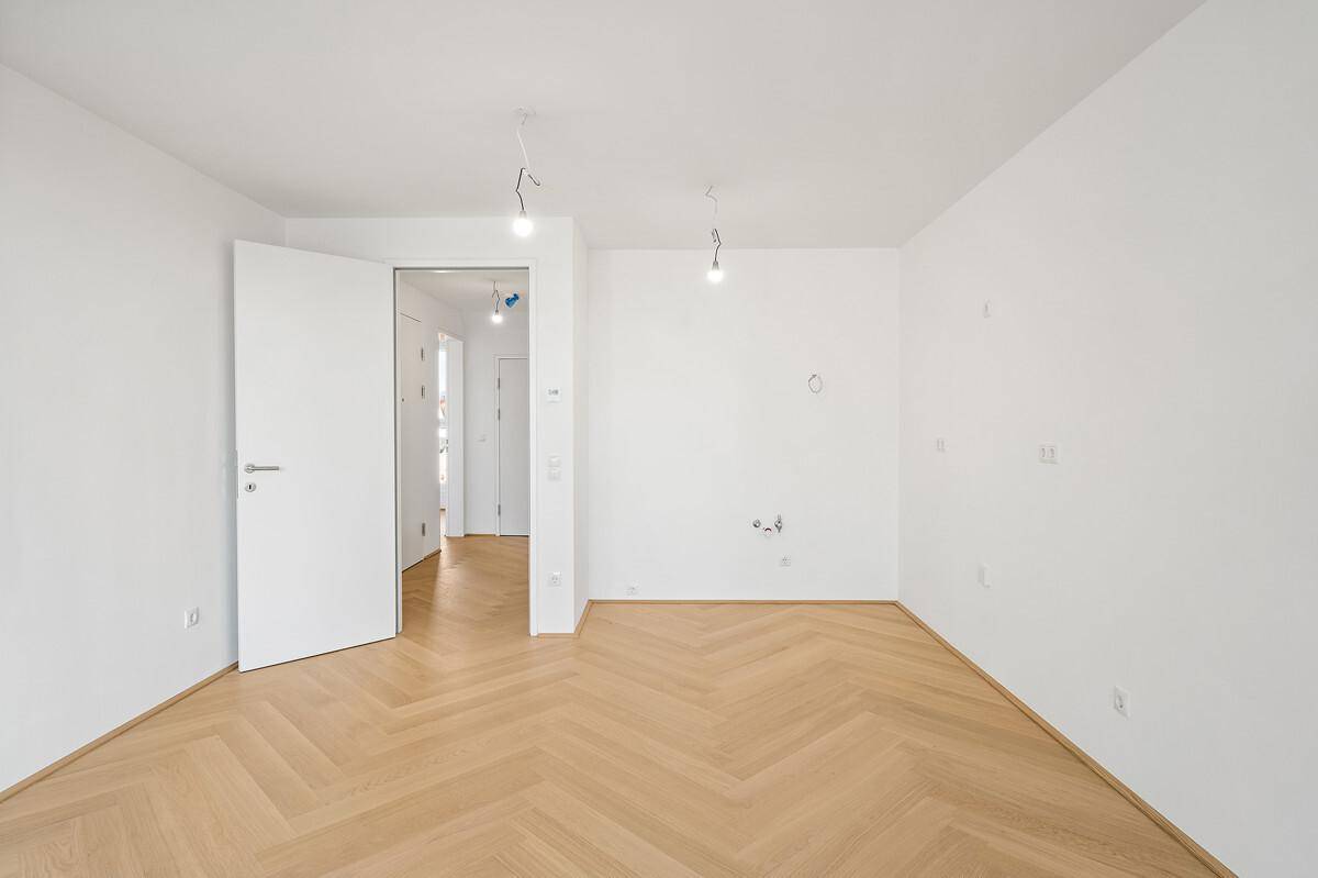 Leeres Zimmer mit hellem Fischgrätparkett und weiß gestrichenen Wänden, bereit zum Einzug.