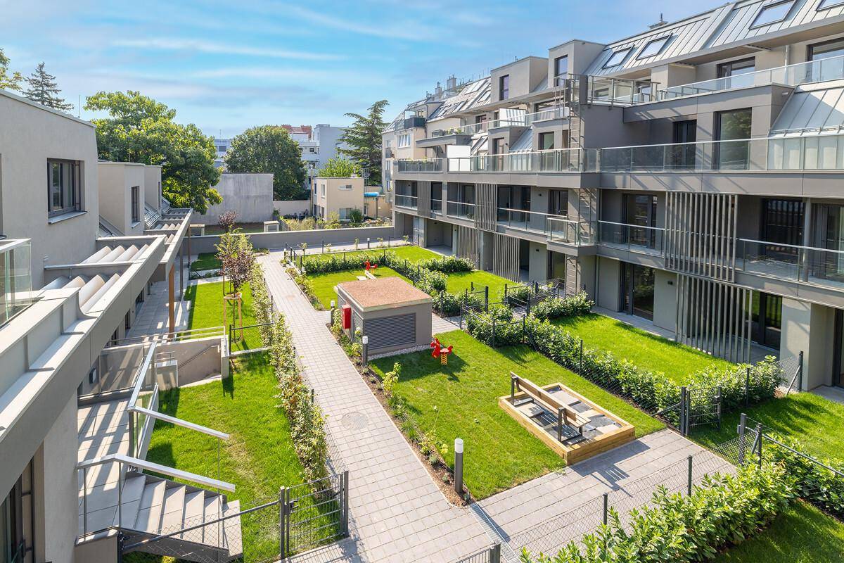 Weitläufige Außenanlage einer Wohnsiedlung mit Gehwegen, Rasenflächen und Kinderspielplatz von oben.