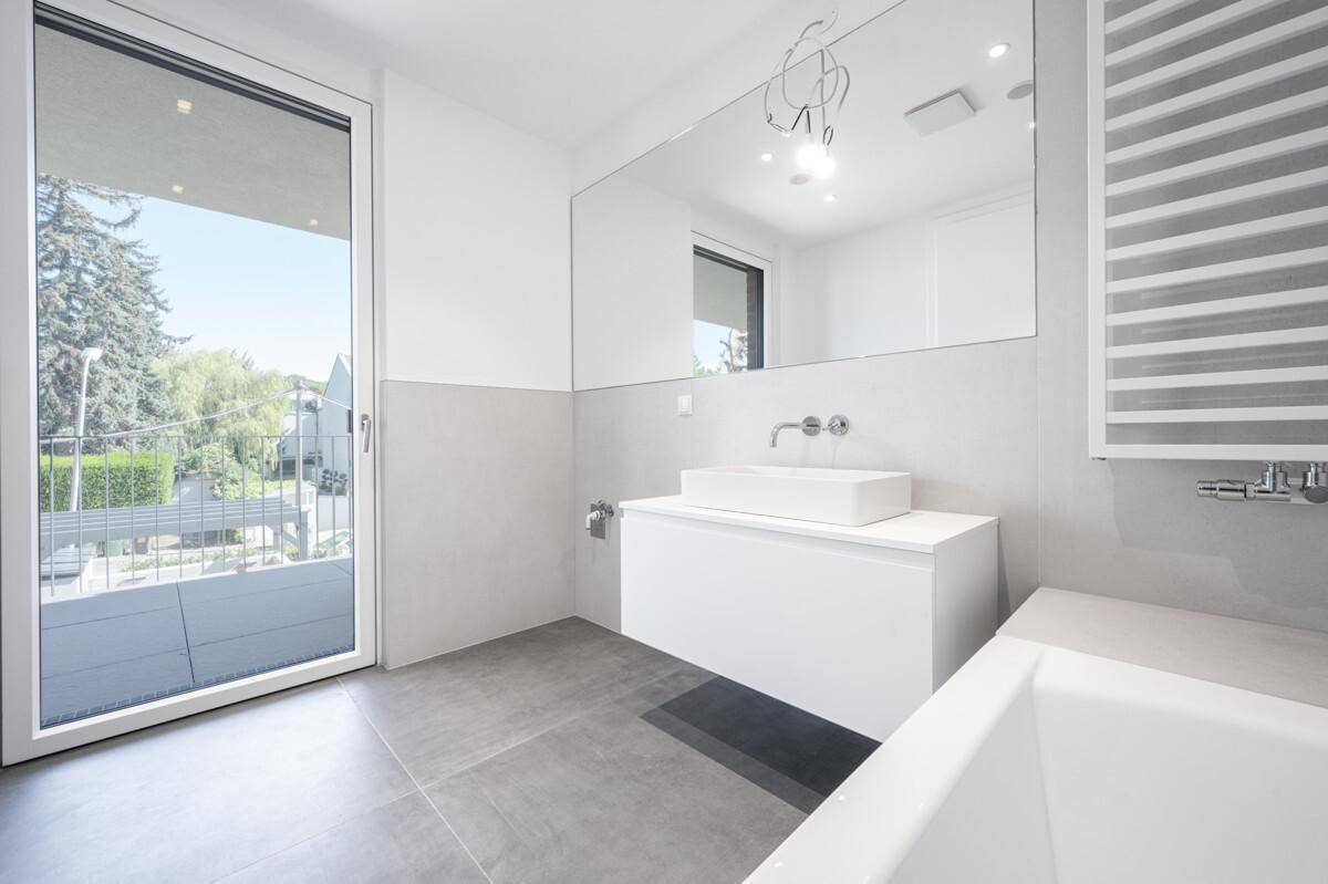 Modernes Badezimmer mit Badewanne, großem Spiegel und Zugang zu einem Außenbereich.