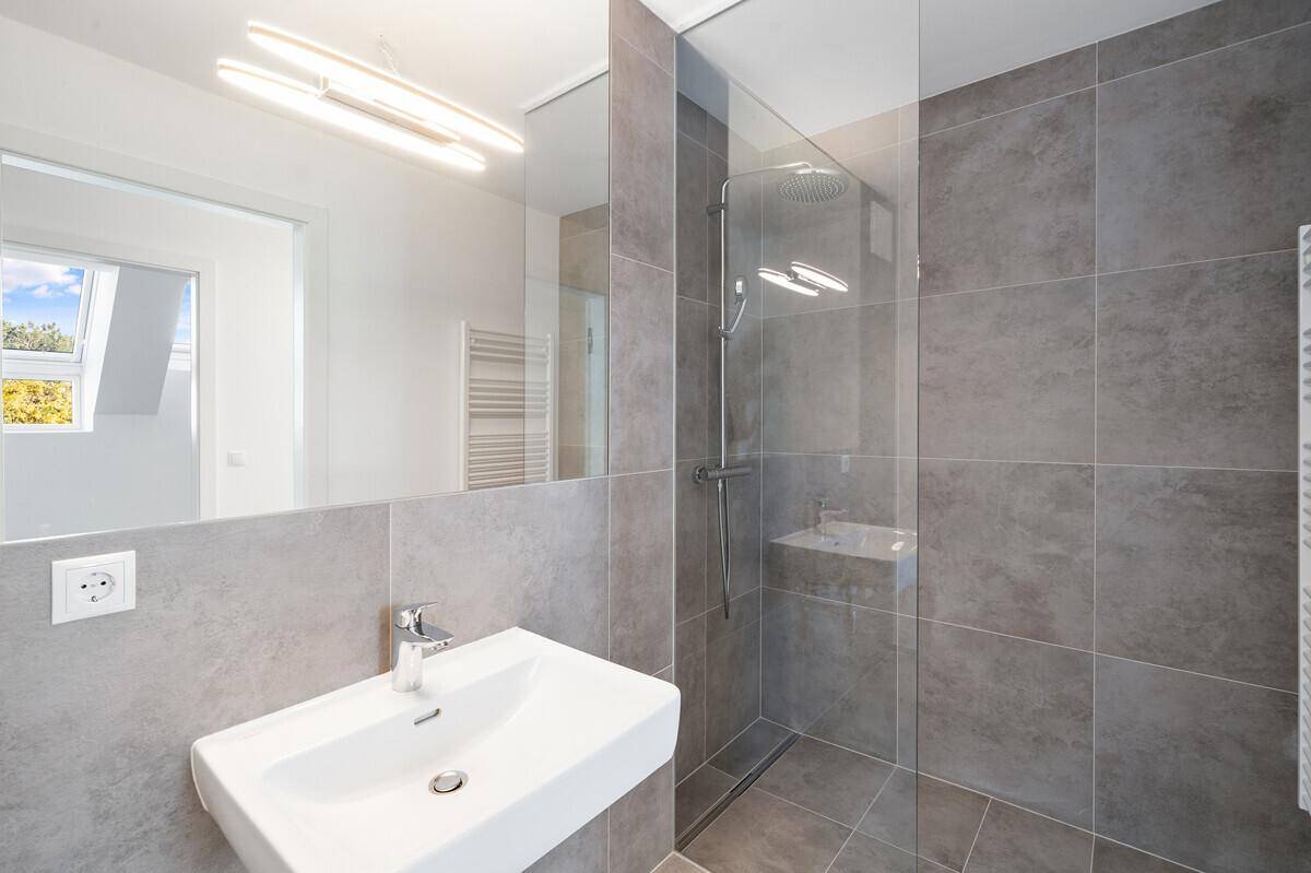 Modernes Badezimmer mit grauen Fliesen, begehbarer Dusche, Einzelwaschbecken und großem Spiegel.