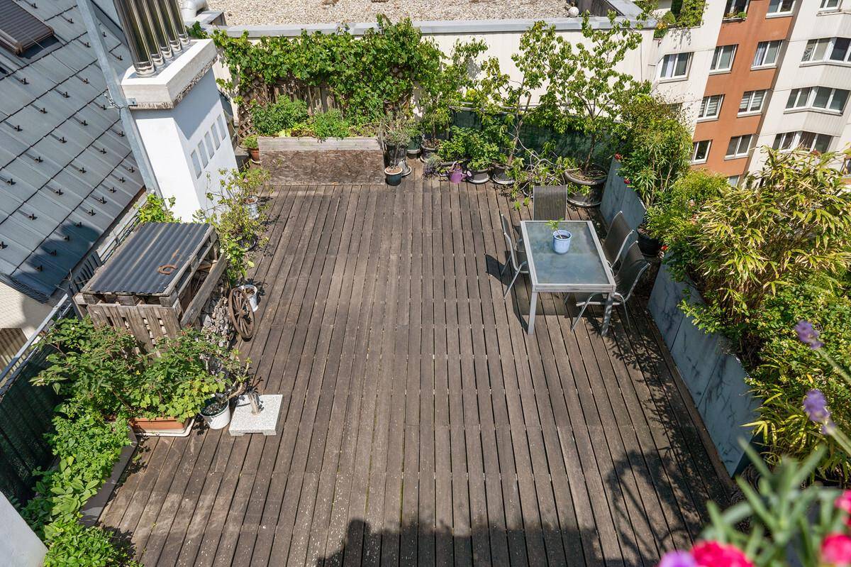 Geräumige Dachterrasse mit Holzboden, Sitzgelegenheiten und Pflanzen.