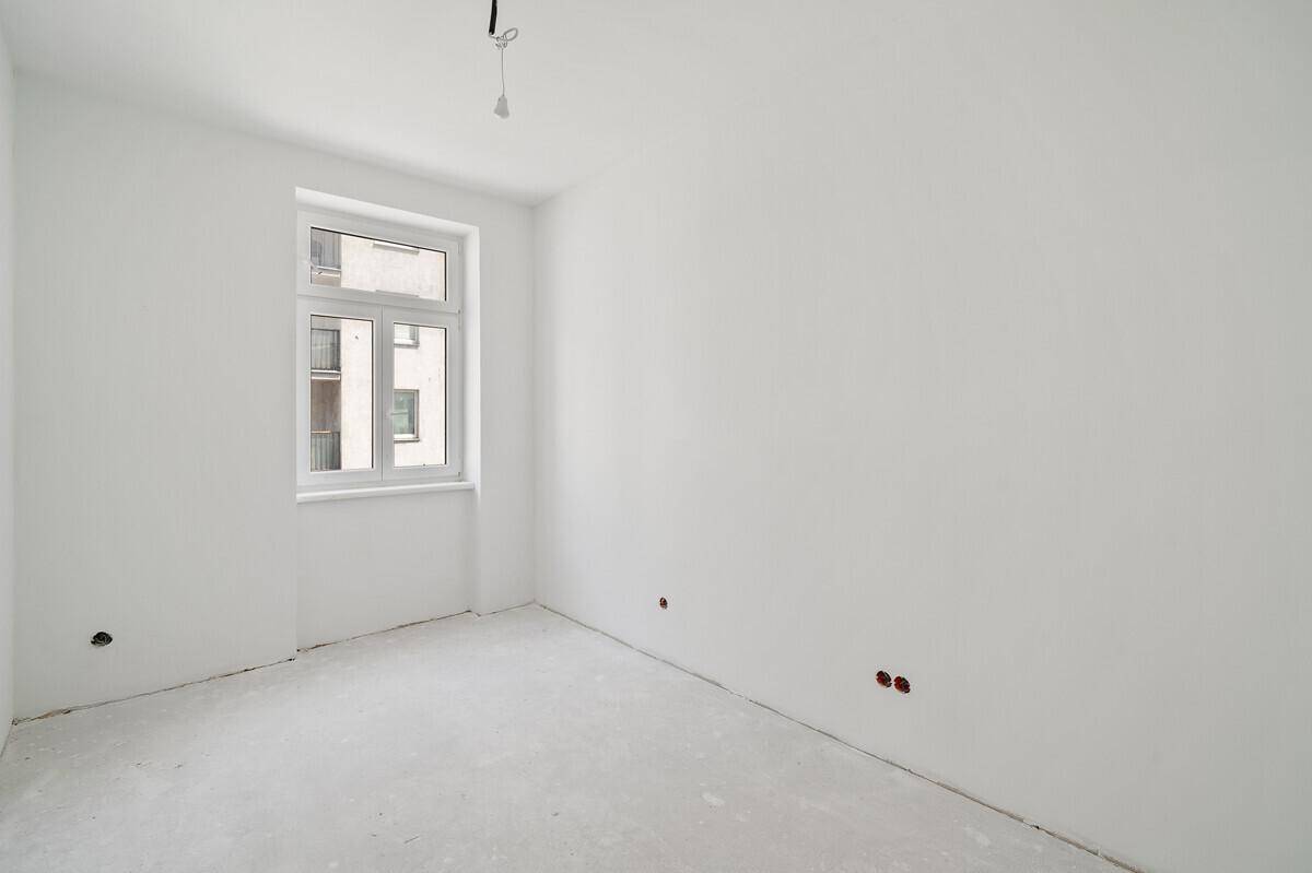 Kleines Schlafzimmer im Rohbau mit einem Fenster und weiß gestrichenen Wänden.