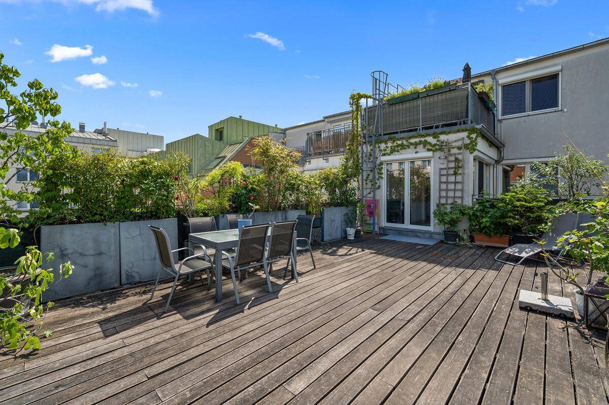 Weitläufige Dachterrasse mit Holzboden, üppiger Bepflanzung und Stadtansicht.