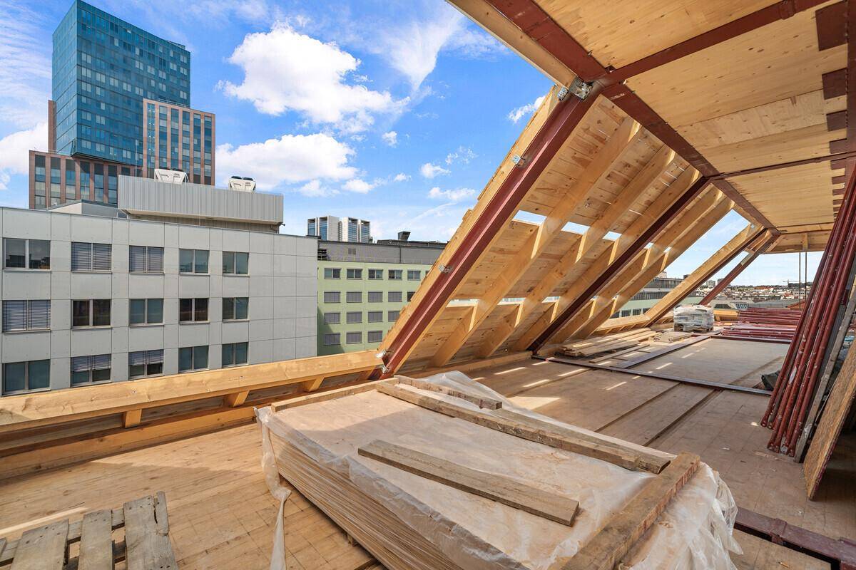 Dachgeschoss im Rohbau mit Holzkonstruktion und Blick auf die umliegende Stadtbebauung.