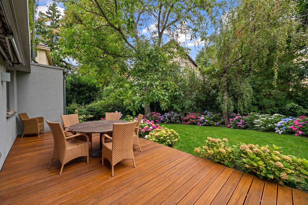 Geräumige Holzterrasse mit Rattanmöbeln, ideal für Entspannung im Grünen, umgeben von blühenden Pflanzen.