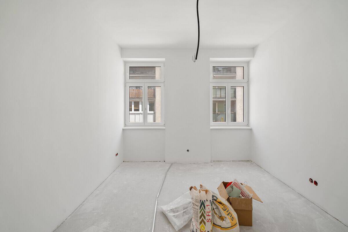 Zimmer im Rohbau mit zwei Fenstern, bereit für den Innenausbau und die Bodengestaltung.