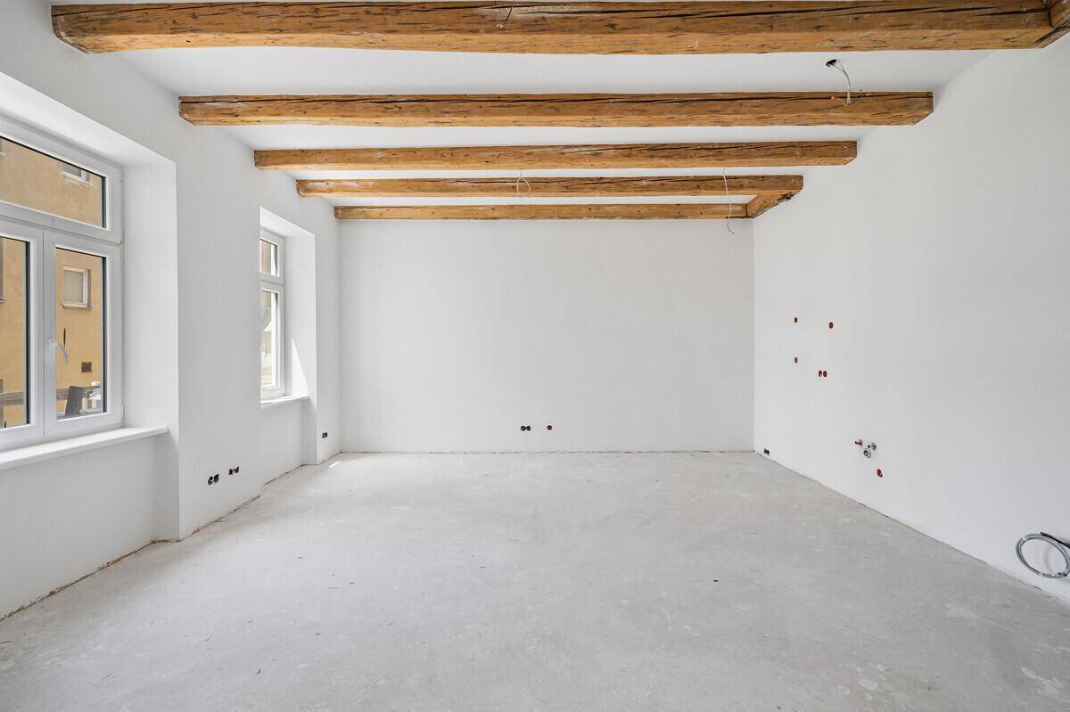 Heller Wohnraum im Rohzustand mit freiliegenden Holzbalken und vielen Fenstern.