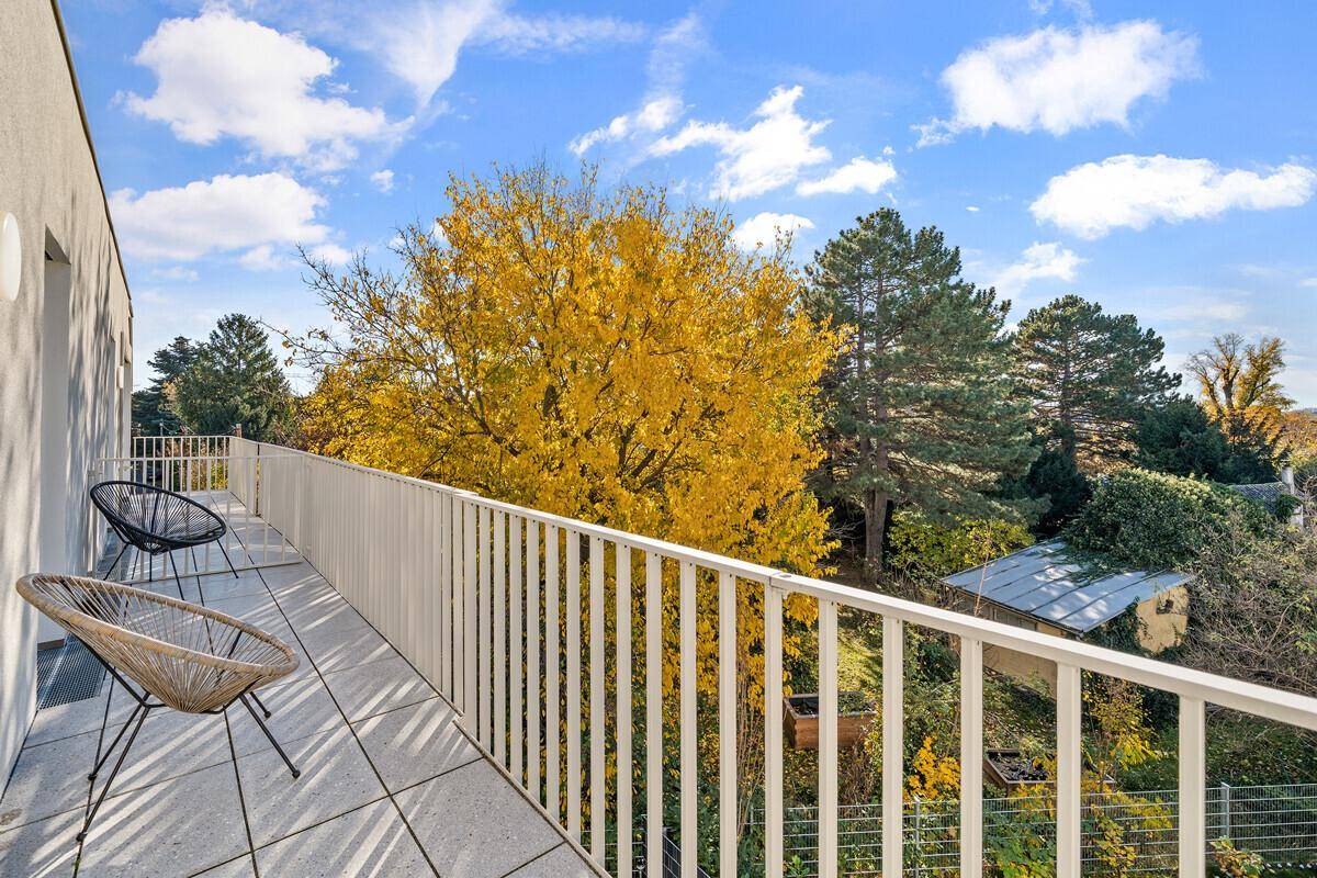 Balkon mit Sitzgelegenheiten, Fliesenboden und Blick auf die herbstliche Natur und die Umgebung.