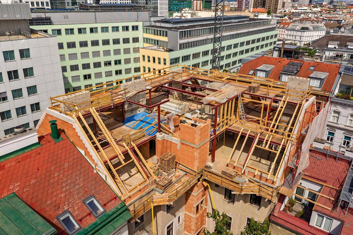 Baustelle auf dem Dach mit sichtbaren Holz- und Stahlkonstruktionen und Stadtblick.