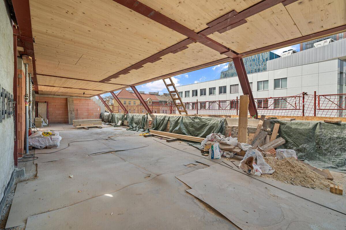 Geräumiges Dachgeschoss im Rohbau mit Baumaterialien und Blick auf die Stadt.