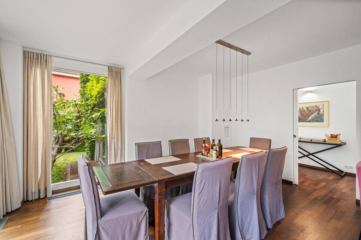 Eleganter Essbereich mit großem Holztisch, bequemen Stühlen und Zugang zum grünen Außenbereich.