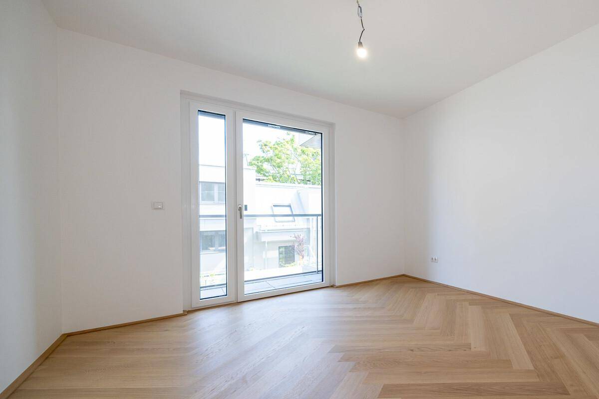 Lichtdurchflutetes Zimmer mit Fischgrätparkett und großem Fenster, bietet vielseitige Nutzungsmöglichkeiten.
