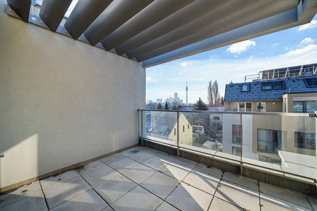 Geräumiger Balkon mit Fliesenboden, Glasgeländer und Blick auf die Stadt und Umgebung.
