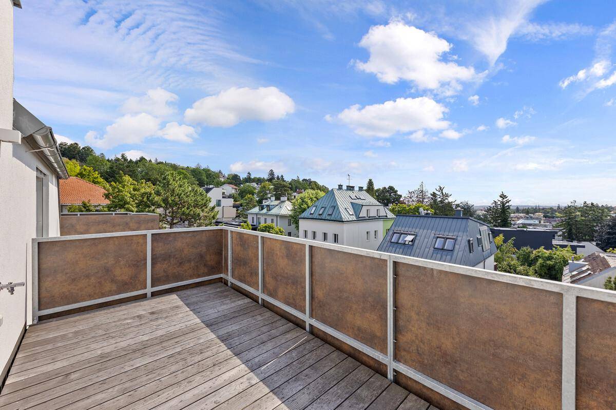 Privater Balkon mit Holzboden und blickdichter Brüstung, umgeben von Grün.