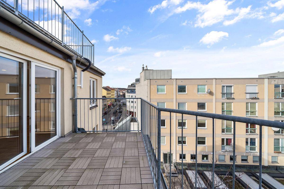 Geräumiger Balkon mit Holzdielen und Metallgeländer, bietet einen Blick auf die Umgebung.