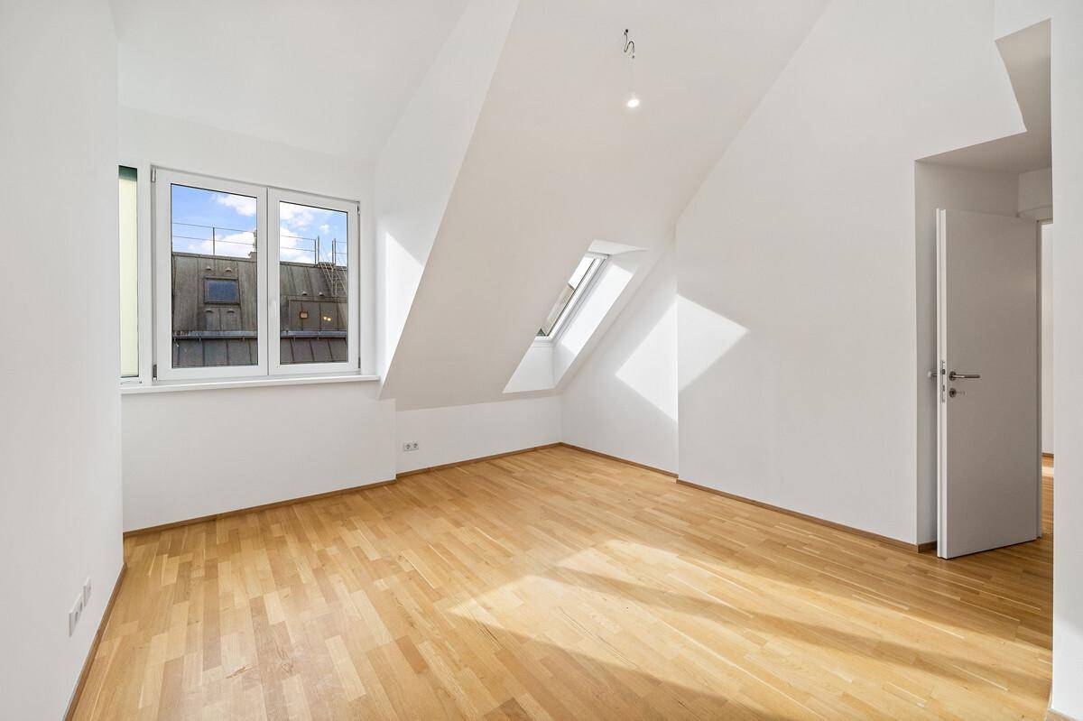 Helles Schlafzimmer im Dachgeschoss mit Parkettboden, Dachfenster und schrägen Wänden.