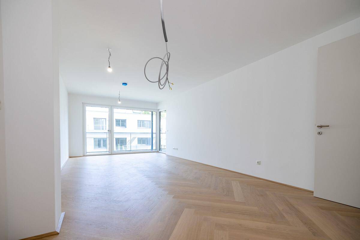 Helles, leeres Zimmer mit Fischgrätparkett und großen Fenstern, bereit für die individuelle Gestaltung.