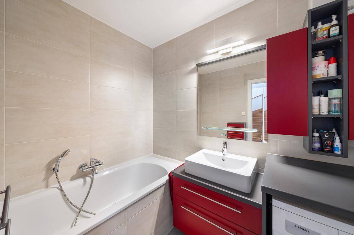 Modernes Badezimmer mit Badewanne, Aufsatzwaschbecken und roten Schränken.