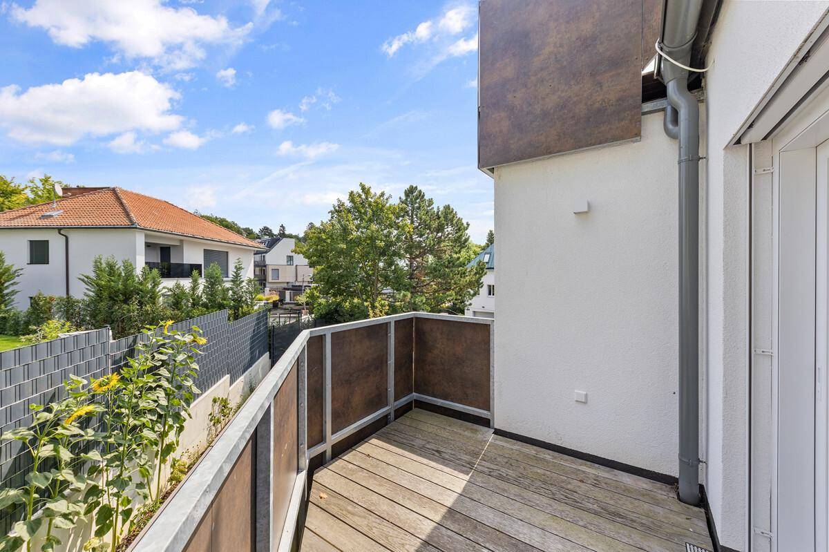 Sonniger Balkon mit Holzboden und Blick auf die umliegende, grüne Nachbarschaft.