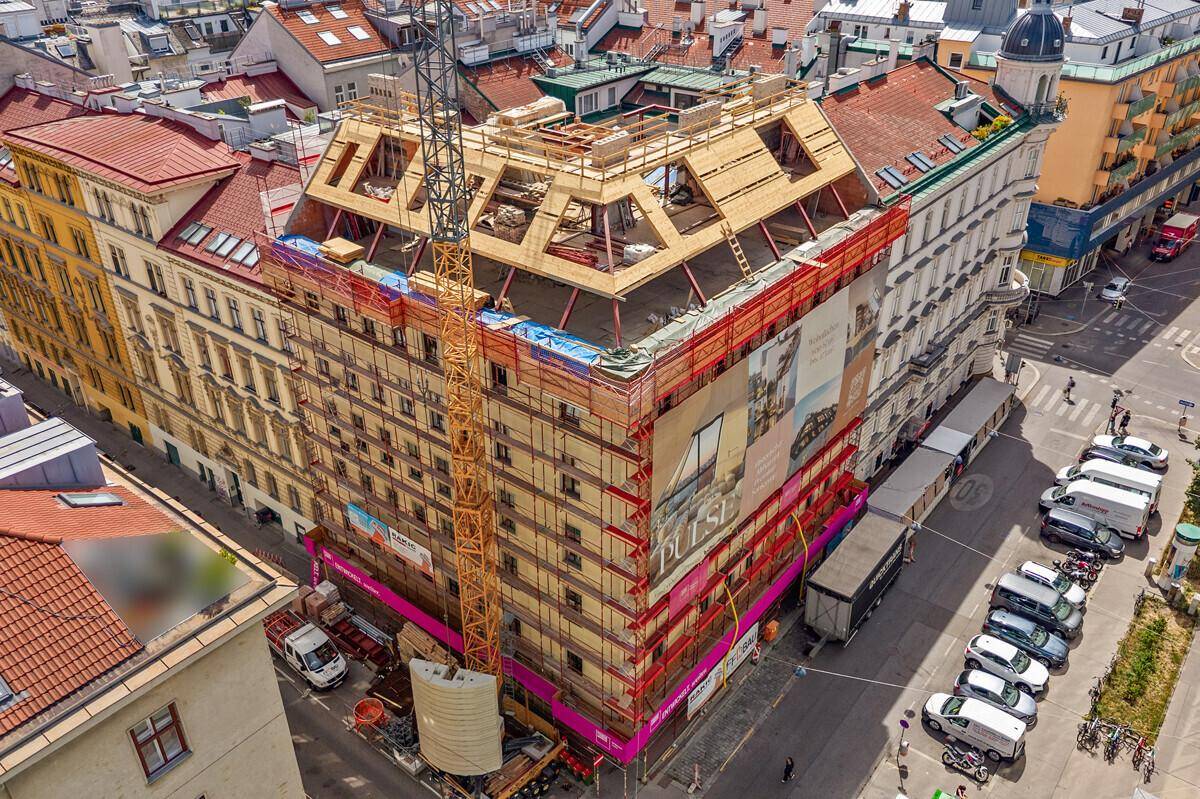 Vogelperspektive auf die Baustelle eines Gebäudes mit Gerüst und umliegender Stadtbebauung.