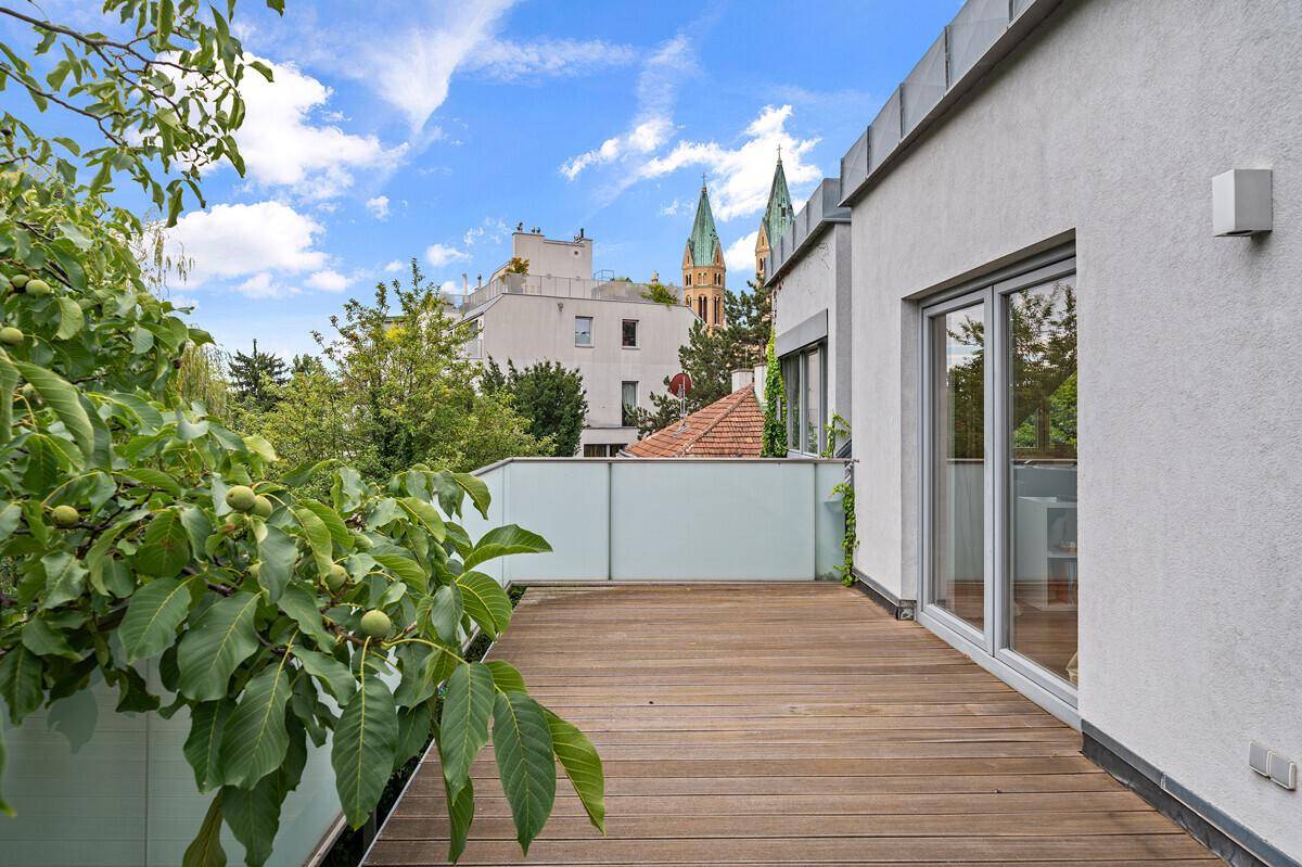 Großer Balkon mit Holzboden und Blick auf die Stadt und eine Kirche, umgeben von Bäumen.