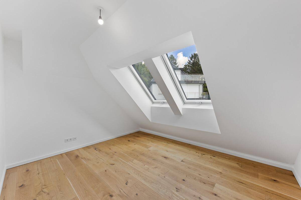 Dachgeschosszimmer mit Holzboden und zwei Dachfenstern, die viel Licht hereinlassen.