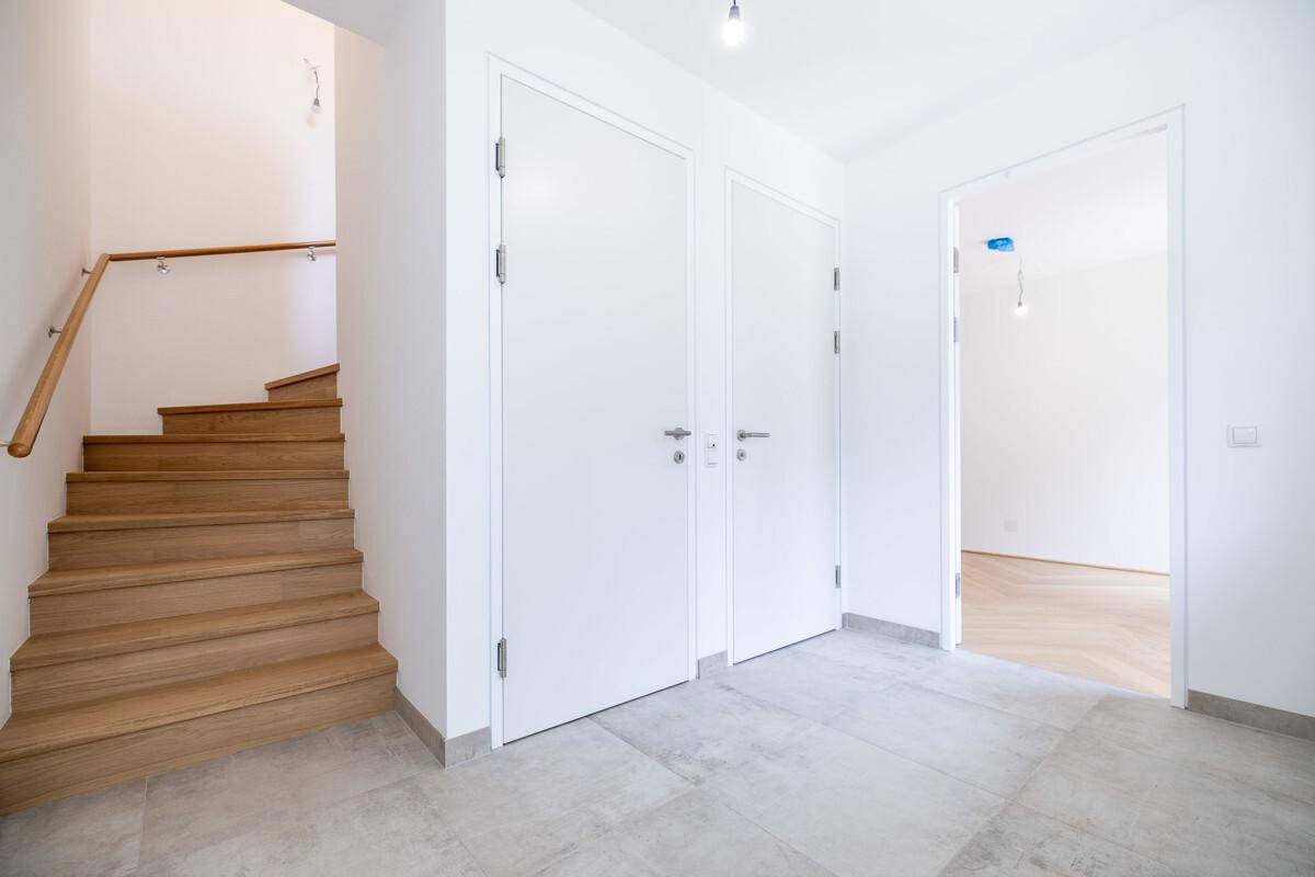 Moderner Eingangsbereich mit Holztreppe und Fliesenboden, der zu den oberen Etagen führt.