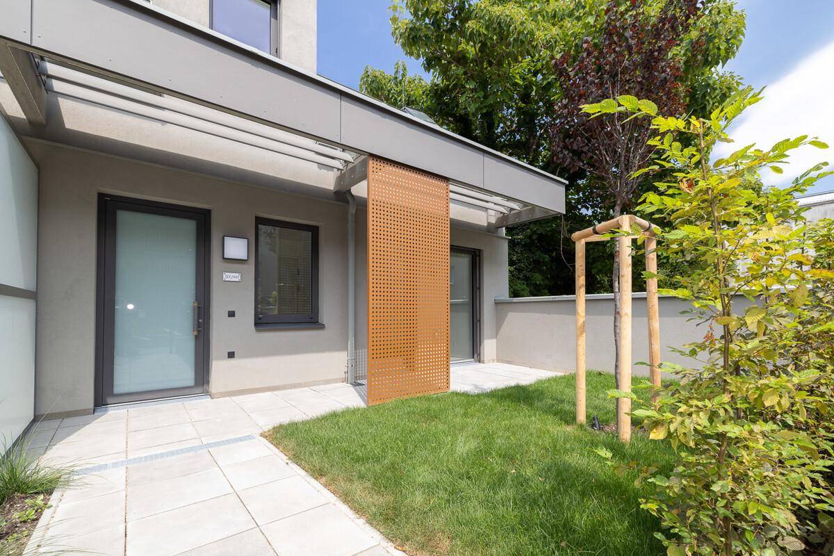 Private Terrasse im Erdgeschoss mit kleinem Rasenbereich und modernem Sichtschutz aus Holz.