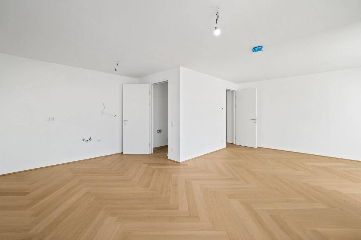 Geräumiger, heller Raum mit Fischgrätparkett und mehreren Türöffnungen in einem Neubau.