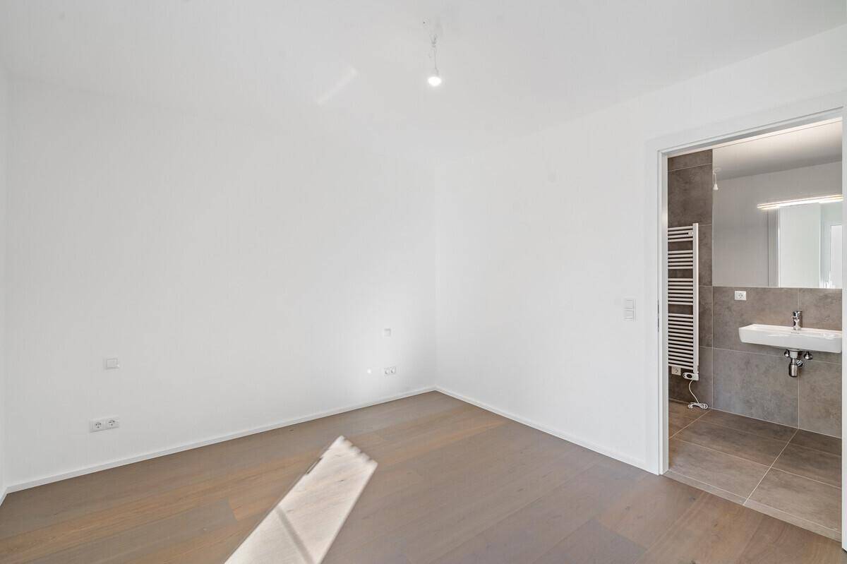 Schlafzimmer mit Holzboden und direktem Zugang zu einem modernen Badezimmer.