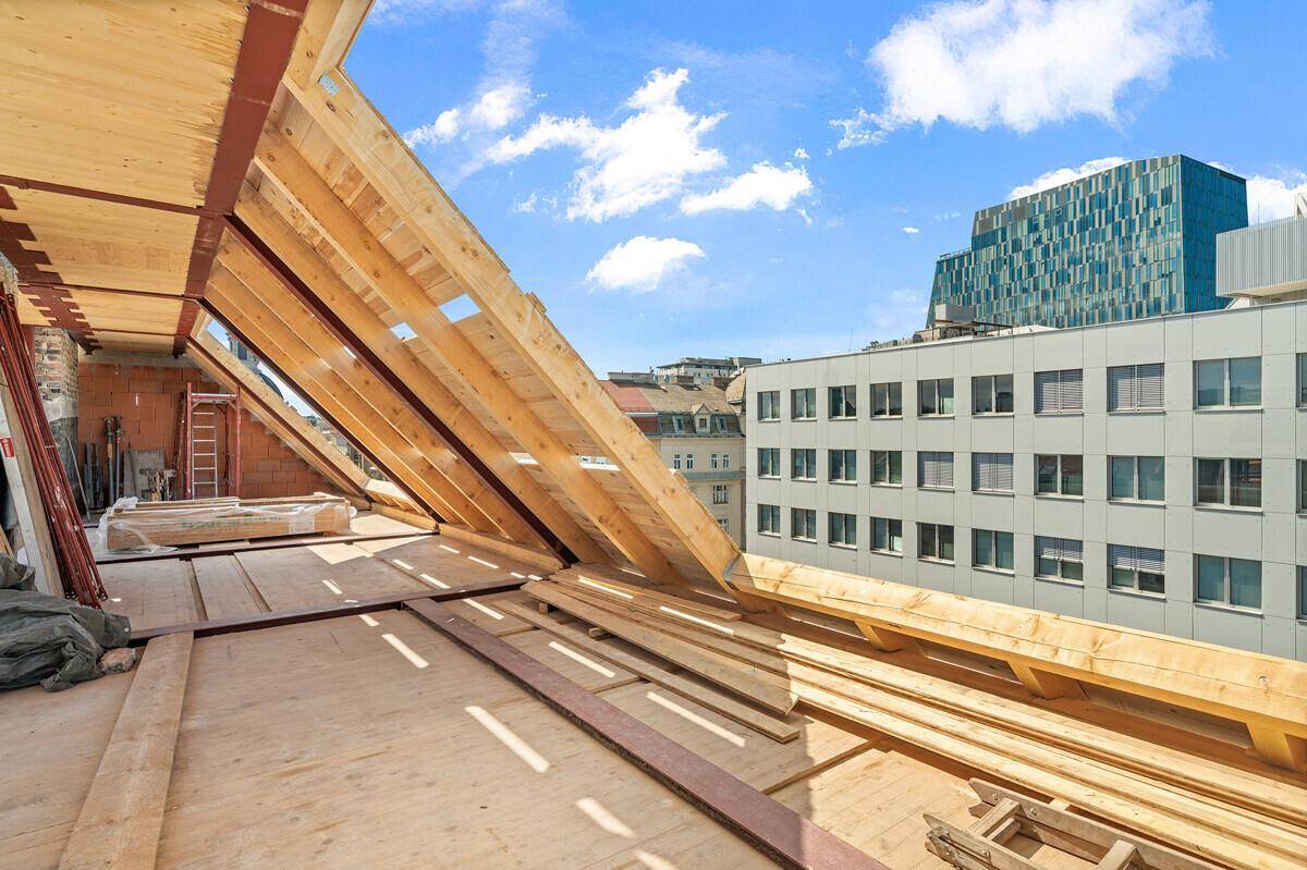 Unfertiges Dachgeschoss mit Holzdachstuhl und Blick auf moderne Gebäude in der Ferne.