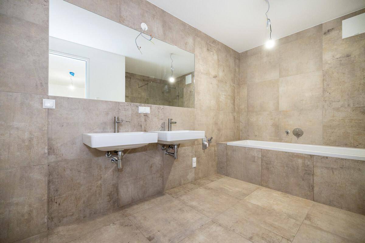 Modernes Badezimmer mit Doppelwaschbecken, Badewanne und großem Spiegel, in neutralen Erdtönen gehalten.