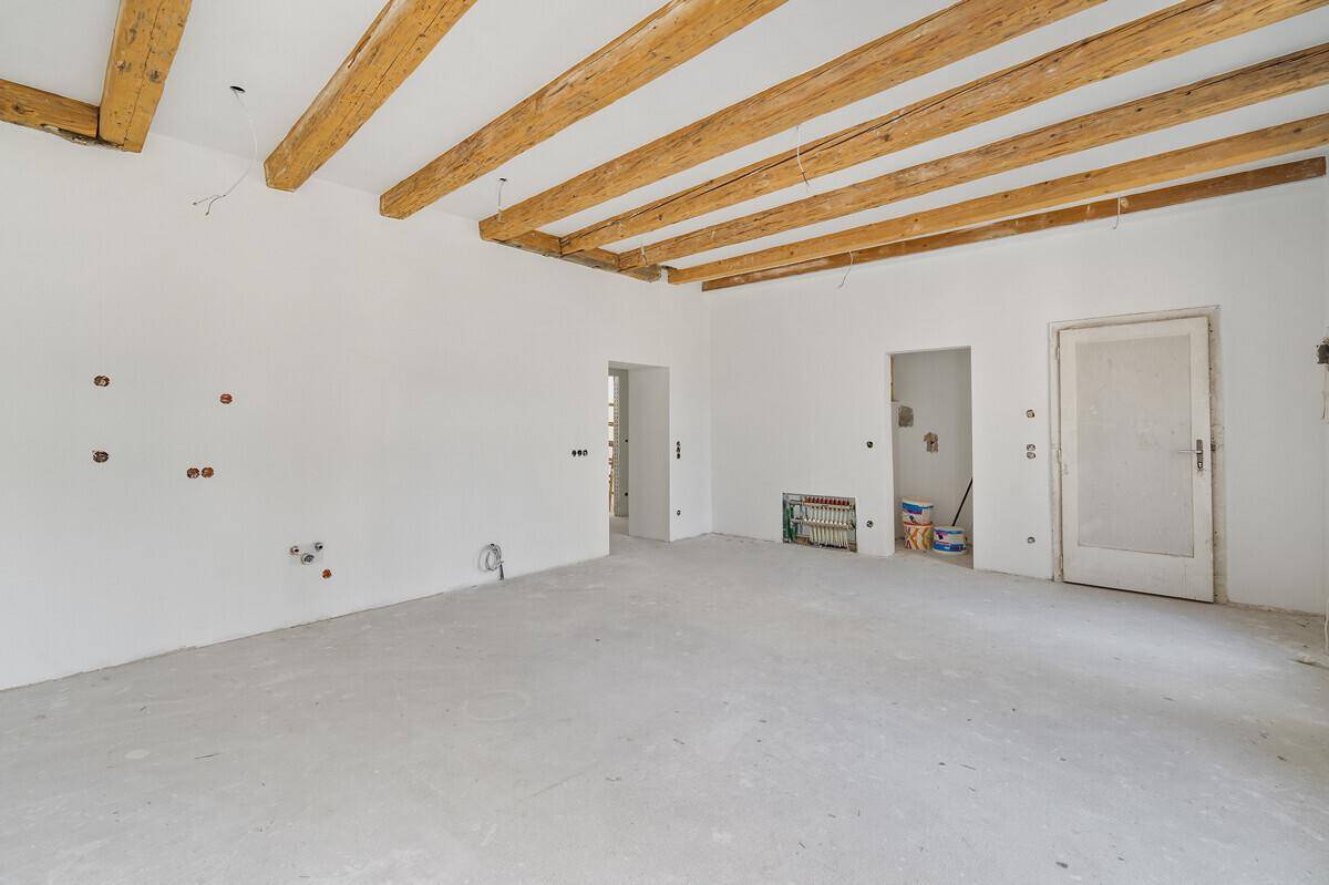 Offener Wohnbereich mit Holzbalken und vorbereiteten Anschlüssen für die weitere Gestaltung.