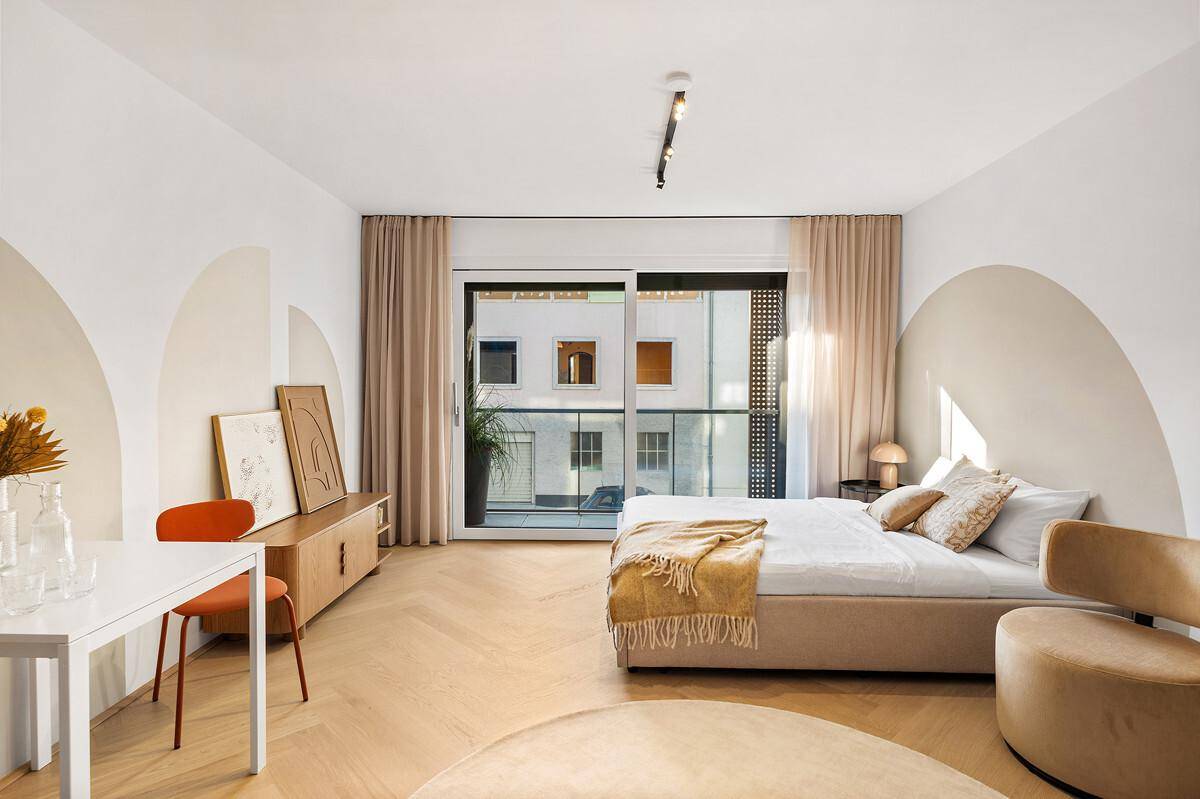 Geräumiges Schlafzimmer mit Holzboden, großen Fenstern und direktem Zugang zu einem Balkon.