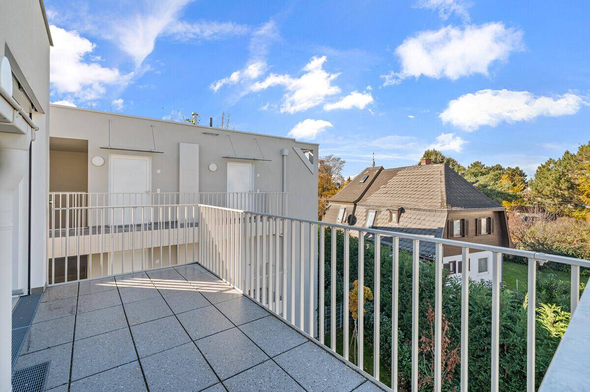 Geräumiger Balkon mit Fliesenboden und weißem Geländer, bietet einen grünen Ausblick auf die Umgebung.