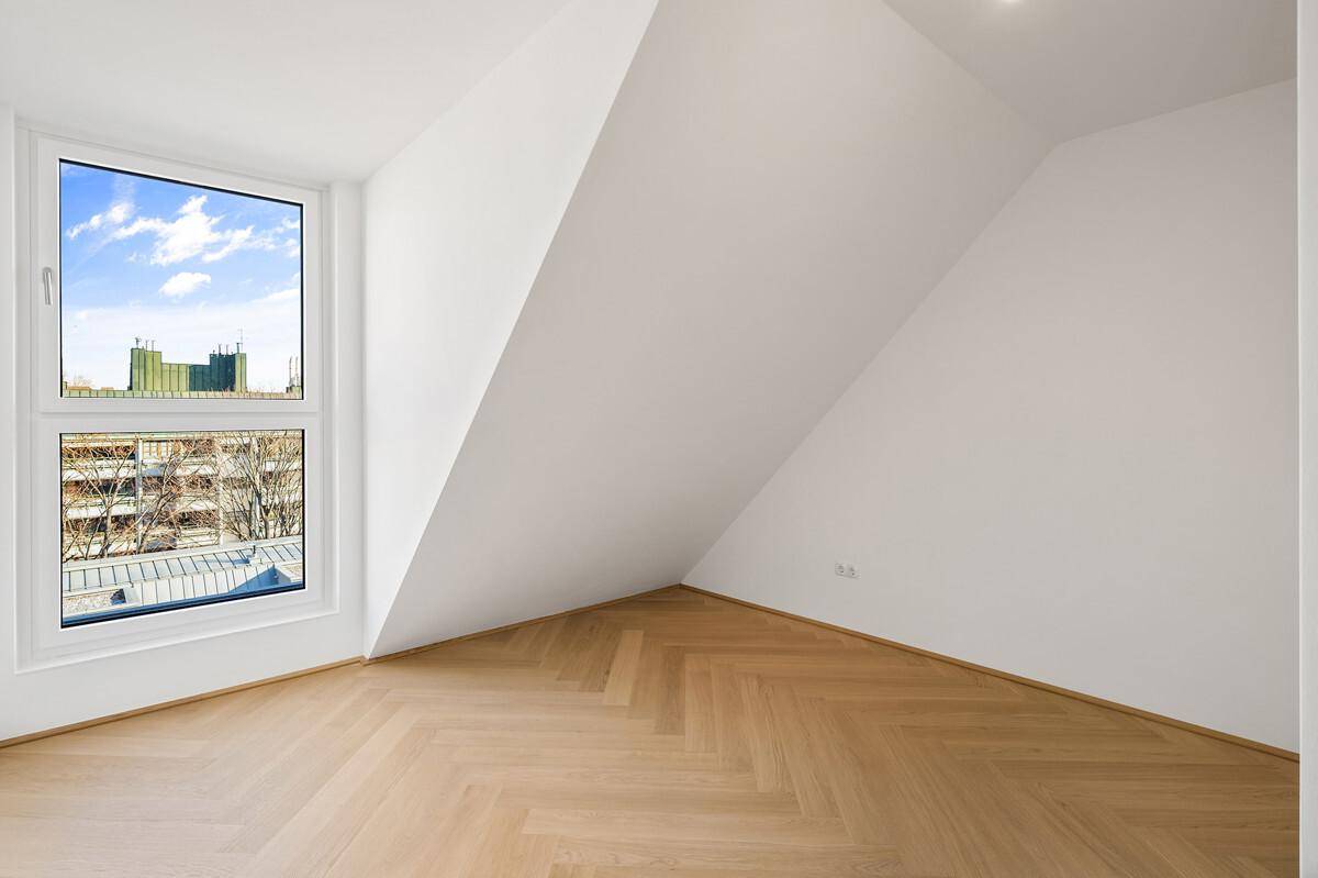 Heller Raum mit Dachschräge, großem Fenster und neuem Fischgrätparkett im Dachgeschoss.