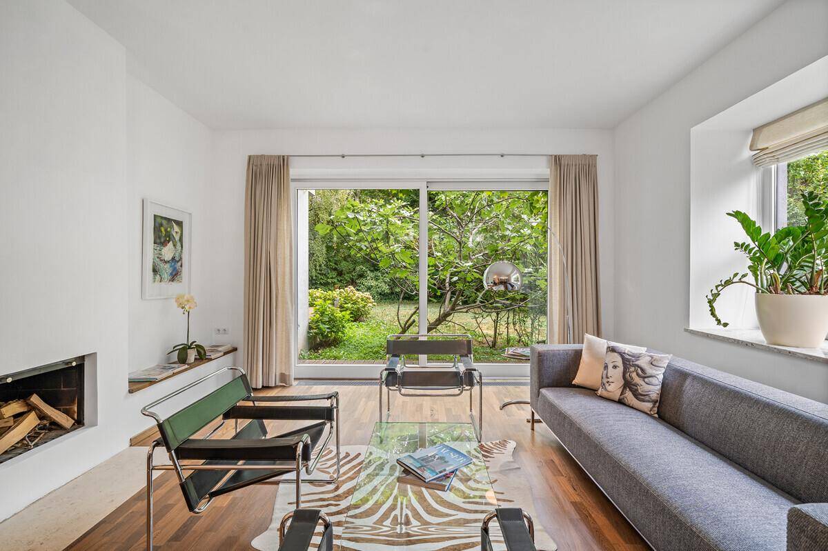 Gemütliches Wohnzimmer mit Kamin, Holzboden und großen Fenstern mit Blick auf den Garten.